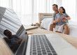 © Bangkok Click Studio - Father sitting on bed in ome bedroom and hugging his mixed-race son with a happy and joyful pose with a reflection on a notebook computer screen