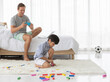 © Bangkok Click Studio - Father using smartphone to take photos of his mixed-race son who playing with a colorful wooden block in home bedroom. Idea for lifestyle of working from home
