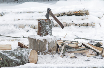 an axe stuck in a tree stump against a background of firewood