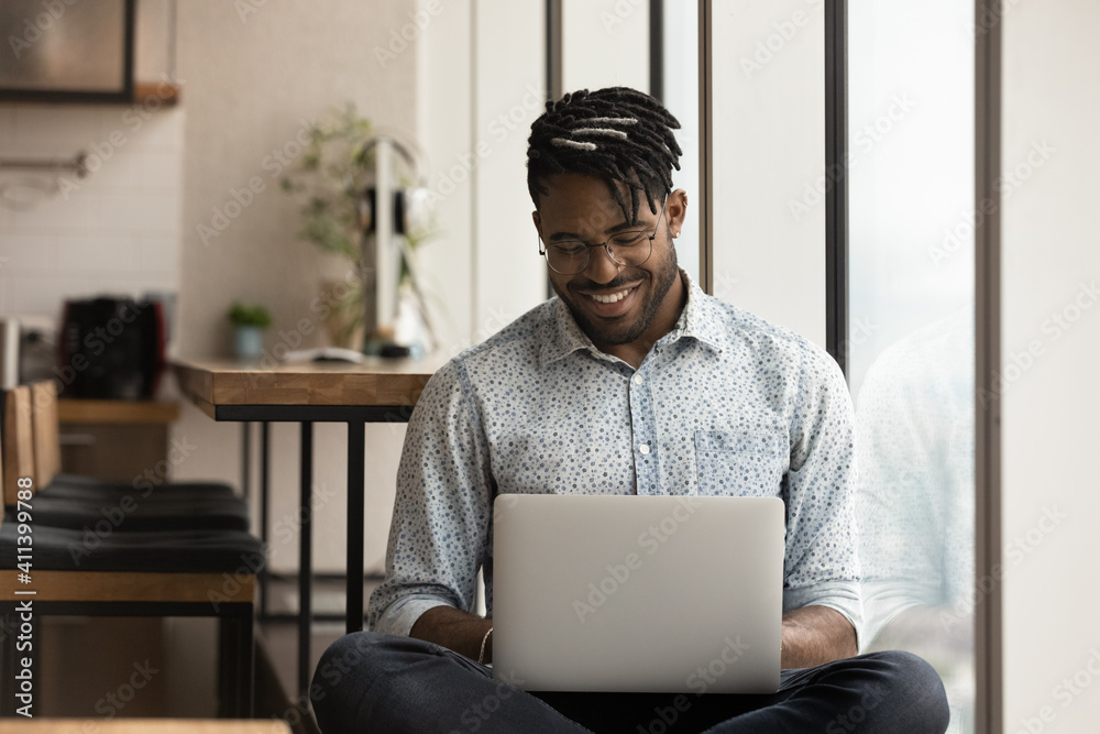 Skilled african man freelancer sit in comfortable pose work from home consult client by video link write programme code on pc. Young black guy relax at home with laptop post comments at social network - obrazy, fototapety, plakaty 