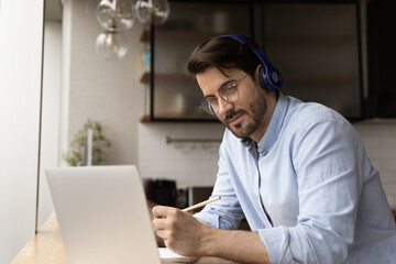 Wall Mural - attentive left handed man in wireless headset look on laptop pc screen watch webinar video lecture h