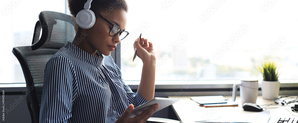 Beautiful african american woman is working using digital tablet while sitting in creative office. - obrazy, fototapety, plakaty 