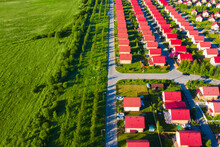 Country Houses Stand In Even Rows. Small Cottages With Red Roof. Countryside Village From A Bird's Eye View. Suburban Village Next To A Green Field. Concept - Buying A House In Countryside Suburbia