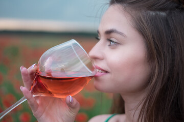 Wall Mural - Young beautiful brunette smiling, relaxing in nature, holding a glass of red wine, enjoying a summer evening, outdoors, dressed in summer clothes.