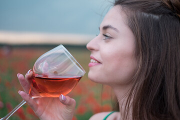 Wall Mural - Young beautiful brunette smiling, relaxing in nature, holding a glass of red wine, enjoying a summer evening, outdoors, dressed in summer clothes.