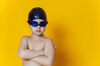 © saulich84 - child athlete wearing blue swimming goggles and a black rubber cap stands in the studio on a yellow background