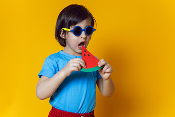 baby boy in red pants eats a paper watermelon on a yellow background