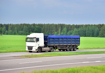 Wall Mural - Truck with tipper semi trailer driving along highway on the green agriculture field background. Modern Dump Semi-Trailer Rear Tipper Truck Trailer. Goods Delivery and Services and Transport logistics