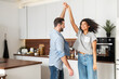 © Vadim Pastuh - Happy young multi ethnic couple in love dancing and holding hands in the kitchen. Joyful boyfriend and girlfriend have a fun at home, newlywed moved in new apartment