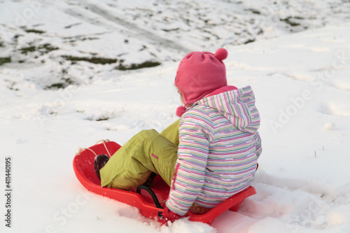 A child on a sled goes down a snow slide. © indigolotos