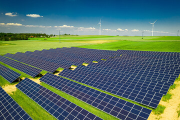 Solar panels and wind turbine on green field, aerial view