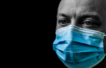 Wall Mural - Sick man with bright blue eyes wearing a facemask, portrait isolated on black with shallow depth of field.