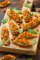 Sweet potato toast loaded with avocado guacamole and baked chickpeas sprinkled with chili flakes served on wooden board