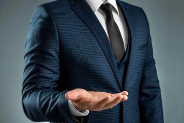 Male hand in a suit shows a palm up gesture on a gray background. Concept of request, bankruptcy, close-up.