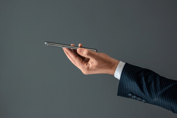 The hand of a businessman in a business suit holds a smartphone horizontally side view. Close-up.
