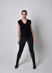 Poster - Simple full length portrait of woman with red hair in a ponytail, wearing casual black tshirt and jeans. Standing pose front on with hand reaching gestures, against a  studio background.