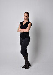 Sticker - Simple full length portrait of woman with red hair in a ponytail, wearing casual black tshirt and jeans. Standing pose facing front on, against a  studio background.