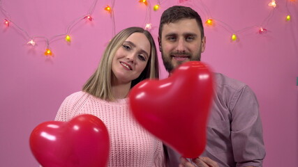 A man and a woman in love look at you and hold heart-shaped balloons. Valentine's Day