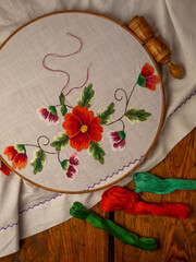 Wall Mural - Flowers embroidery on white textile in hoop wooden background. Traditional ukrainian floss stitch embroidery motifs. Handmade ethnic clothes towel tablecloth. New normal lockdown hooby crafts tutorial