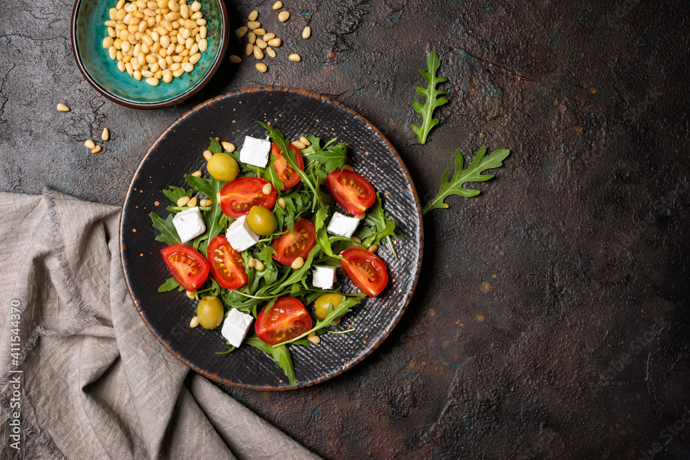 Healthy vegetarian salad with fresh arugula, cherry tomatoes, soft cheese, olives and pine nuts - obrazy, fototapety, plakaty 