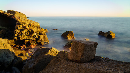 sunset at sea with sunlight bathing the rocks and long exposure photography with silky water. Spain.