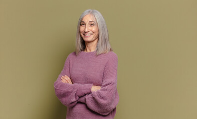 Wall Mural - senior woman smiling to camera with crossed arms and a happy, confident, satisfied expression, lateral view