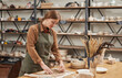 Portrait of young female artisan making plant imprint ceramics on wooden table in pottery workshop, small business and hobby concept, copy space