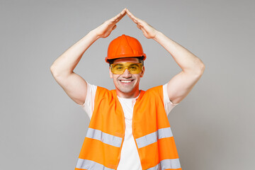 Poster - Young employee man in orange vest protective hardhat hold folded hands above head like roof stay home isolated on grey background studio Instruments for renovation apartment room. Repair home concept.