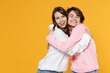 © ViDi Studio - Smiling cheerful two young women friends 20s wearing casual basic white pink hoodies standing hugging having fun looking camera keeping eyes closed isolated on yellow color background studio portrait.