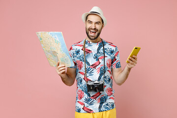 Wall Mural - Laughing young traveler tourist man in summer clothes hat using mobile cell phone hold city map isolated on pink background. Passenger traveling abroad on weekends getaway. Air flight journey concept.