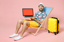 Full Length Smiling Traveler Tourist Man In Hat Sit On Deck Chair Hold Laptop Pc Computer With Blank Empty Screen Isolated On Pink Background. Passenger Travel On Weekend. Air Flight Journey Concept.