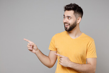 Wall Mural - Young caucasian bearded smiling happy man in yellow basic t-shirt point index finger aside on workspace area copy space mock up isolated on grey background studio portrait People lifestyle concept