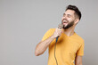 © ViDi Studio - Young caucasian smiling bearded handsome student happy man 20s wearing casual yellow basic t-shirt sing song in microphone enjoying leisure time isolated on grey color background studio portrait.