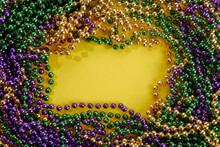 A Frame Of Three Colors Of Mardi Gras Beads On Yellow Background
