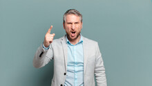 Adult Businessman Pointing At Camera With An Angry Aggressive Expression Looking Like A Furious, Crazy Boss