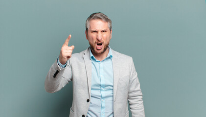 adult businessman pointing at camera with an angry aggressive expression looking like a furious, cra