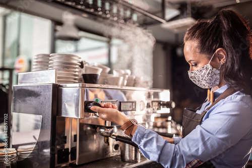 Face mask wearing waitress operates coffee machine in a cafe © weyo