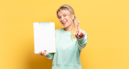 Wall Mural - blonde woman smiling proudly and confidently making number one pose triumphantly, feeling like a leader