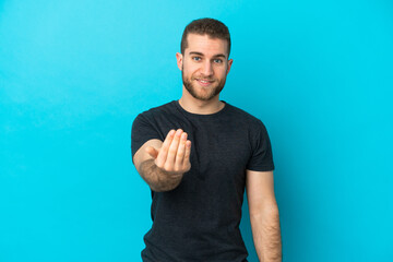 Wall Mural - Young handsome caucasian man isolated on blue background inviting to come with hand. Happy that you came