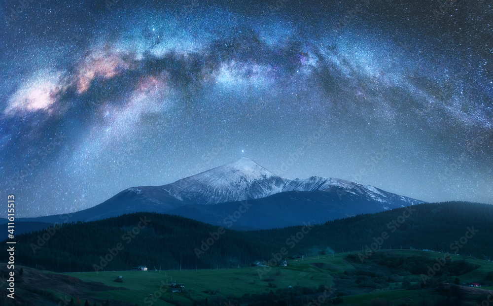 Arched Milky Way over the beautiful mountains with snow covered peak at night in summer. Colorful landscape with bright starry sky with Milky Way arch, snowy rocks, hills. Galaxy. Nature and space - obrazy, fototapety, plakaty 