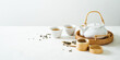 © PINKASEVICH - Asian tea concept mockup, two white cups of tea and teapot surrounded with green dry tea  with space for a text on light background. Wide banner.