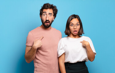 Canvas Print - young couple looking shocked and surprised with mouth wide open, pointing to self