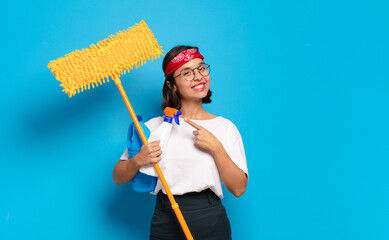 Wall Mural - young latin woman smiling cheerfully, feeling happy and pointing to the side and upwards, showing object in copy space