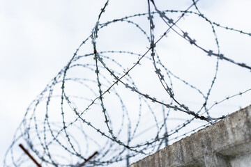 Fence with metal barbed wire again cloudy sky. Protected area, guarded object, prison