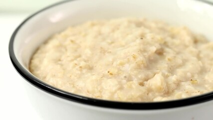 Wall Mural - rotating bowl of freshly made oatmeal porridge for a healthy breakfast, close - up 