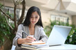 © Prathankarnpap - Businesswoman working with laptop computer and writing something in her schedule book at outdoor workplace.
