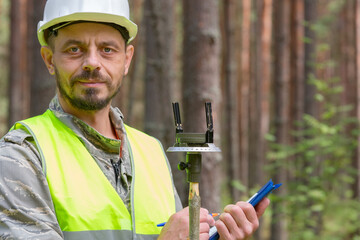 The forester works in the forest with a measuring tool. Real people work in forestry.