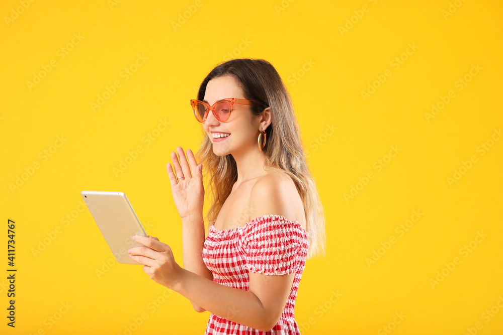 Young woman with tablet computer video chatting on color background