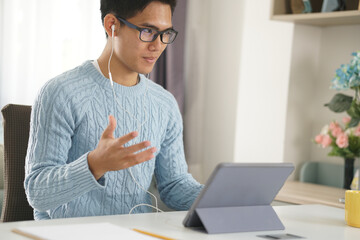 Wall Mural - asian young student man entrepreneur wear earphones working by video call conference studying learning online at home. e-learning webinar meeting. social distance in covid pandemic