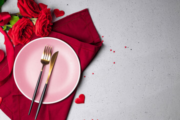 Plate, cutlery and red roses on the gray background, romantic dinner concept. Free space for text